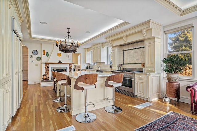 kitchen with pendant lighting, cream cabinets, high end stainless steel range oven, light stone counters, and a tray ceiling