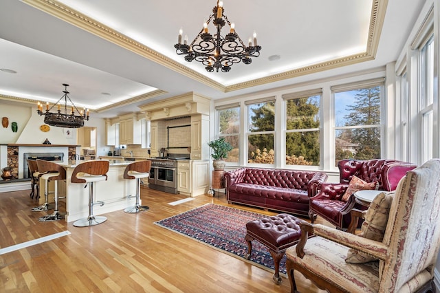 living room with a raised ceiling, crown molding, a chandelier, and light hardwood / wood-style floors