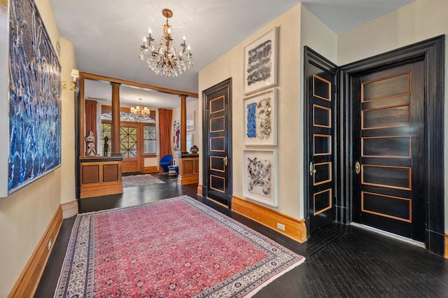 corridor featuring dark wood-type flooring, decorative columns, and a notable chandelier