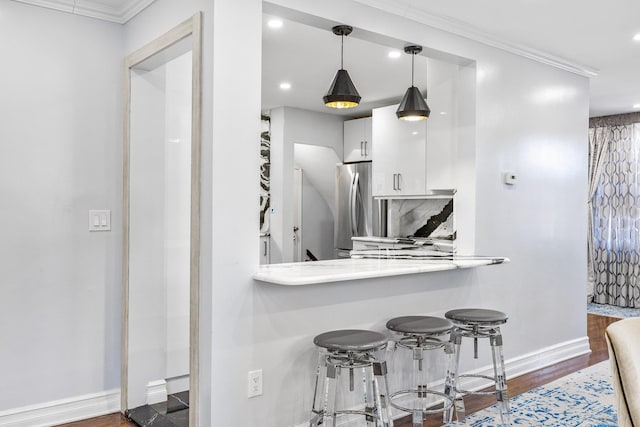 kitchen with stainless steel refrigerator, white cabinetry, a kitchen breakfast bar, crown molding, and decorative light fixtures