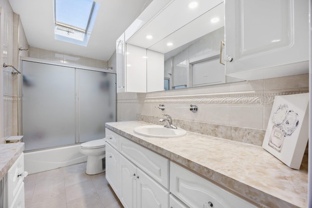 full bathroom featuring a skylight, combined bath / shower with glass door, toilet, decorative backsplash, and vanity