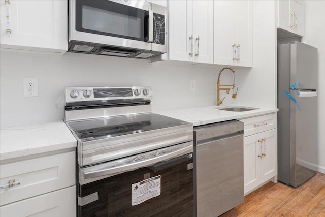 kitchen with appliances with stainless steel finishes, light stone counters, sink, light hardwood / wood-style flooring, and white cabinets