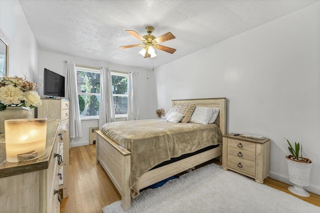 bedroom featuring radiator, ceiling fan, light hardwood / wood-style flooring, and a textured ceiling