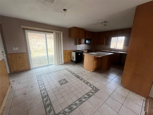 kitchen with a textured ceiling, wooden walls, a kitchen island, sink, and light tile patterned flooring