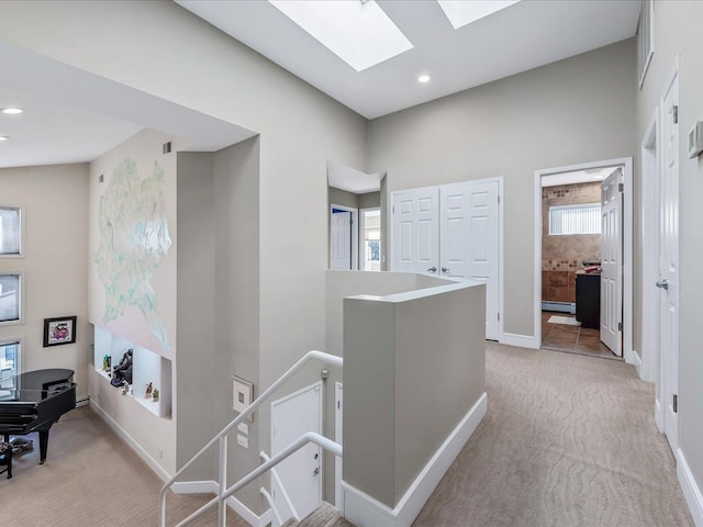 corridor featuring light colored carpet, a baseboard radiator, a skylight, and a healthy amount of sunlight