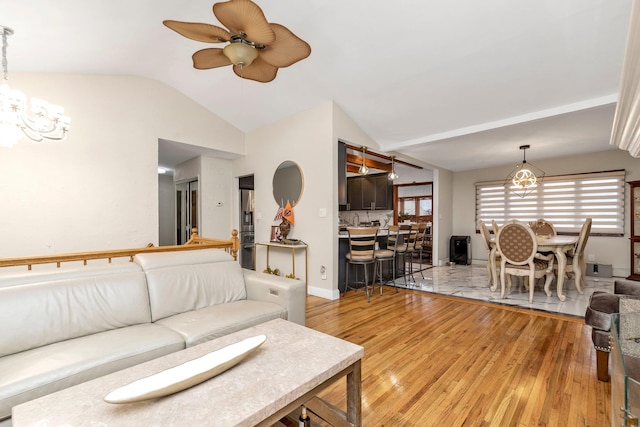 living room featuring ceiling fan with notable chandelier, wood-type flooring, and vaulted ceiling