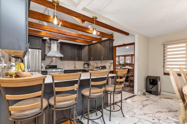 kitchen with tasteful backsplash, stainless steel appliances, wall chimney range hood, beamed ceiling, and hanging light fixtures