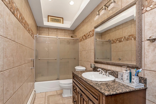 full bathroom with combined bath / shower with glass door, a baseboard heating unit, toilet, vanity, and tile walls