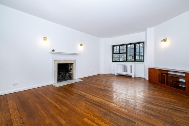 unfurnished living room featuring hardwood / wood-style floors, radiator heating unit, a tile fireplace, and baseboards