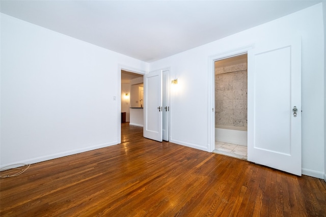 unfurnished bedroom featuring baseboards, wood finished floors, and ensuite bathroom