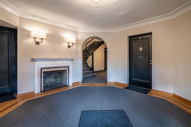 unfurnished living room with arched walkways, a fireplace with flush hearth, a textured ceiling, baseboards, and stairs