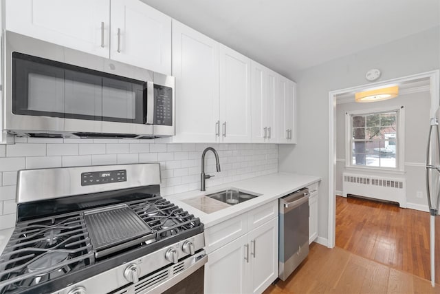 kitchen featuring sink, radiator heating unit, stainless steel appliances, light hardwood / wood-style floors, and white cabinets