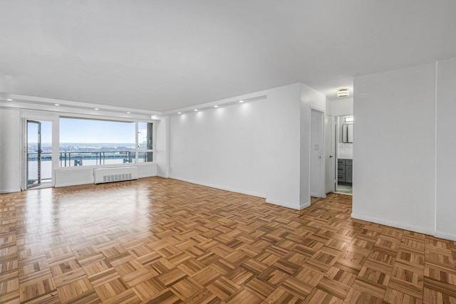 unfurnished living room with parquet flooring, a water view, and radiator