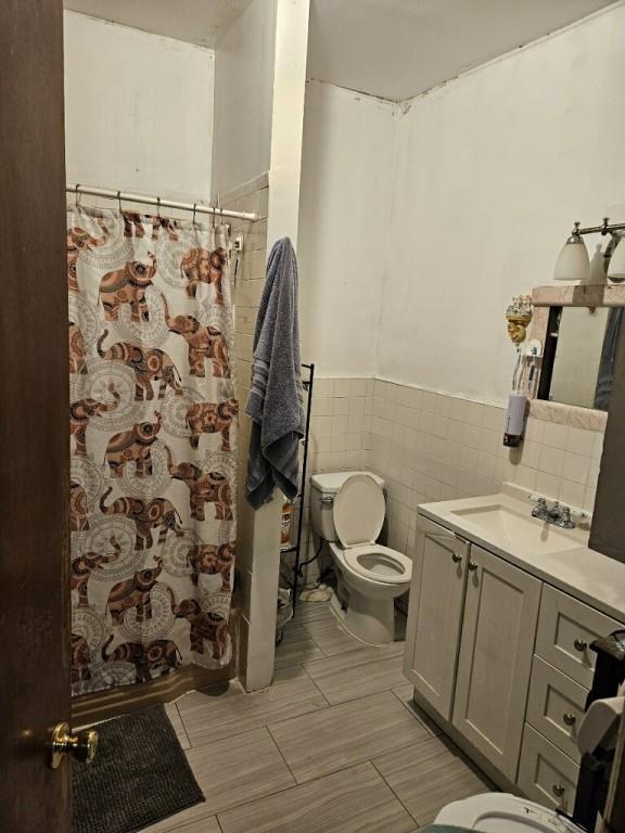 bathroom featuring tile walls, toilet, vanity, and a shower with curtain