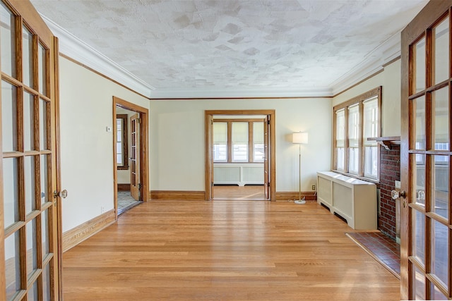 empty room with ornamental molding, radiator heating unit, light hardwood / wood-style floors, and french doors