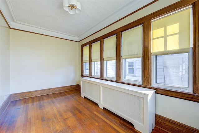 spare room with crown molding, dark wood-type flooring, radiator heating unit, and a textured ceiling