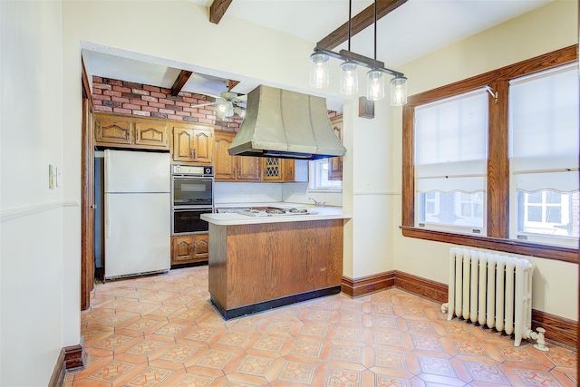 kitchen featuring white appliances, hanging light fixtures, radiator heating unit, island exhaust hood, and kitchen peninsula