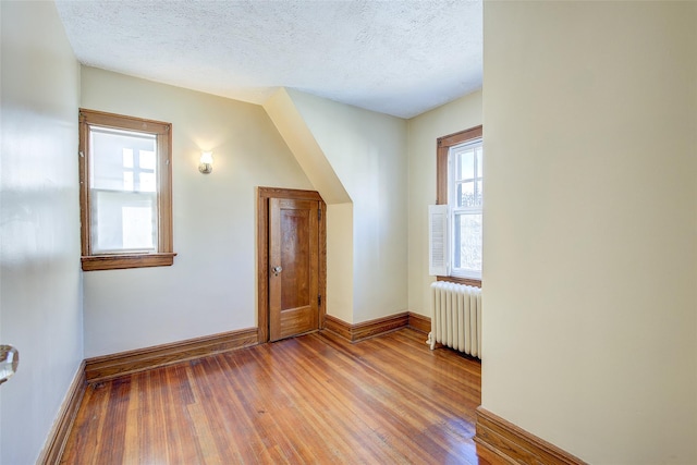 additional living space featuring radiator heating unit, wood-type flooring, and a textured ceiling