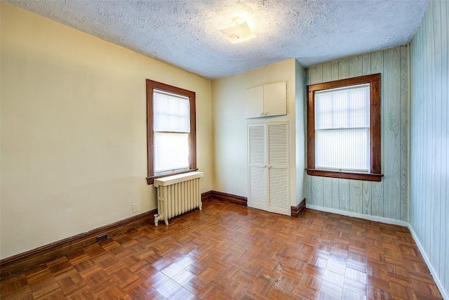 unfurnished room featuring dark parquet flooring, radiator, and a textured ceiling