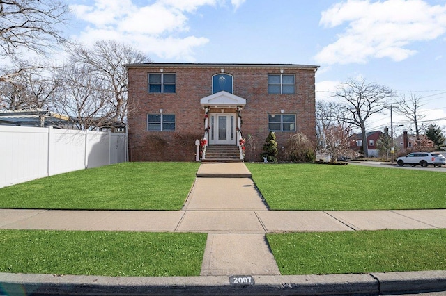 colonial home with brick siding, a front yard, and fence