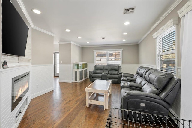 living area with a wainscoted wall, visible vents, dark wood finished floors, a fireplace, and ornamental molding