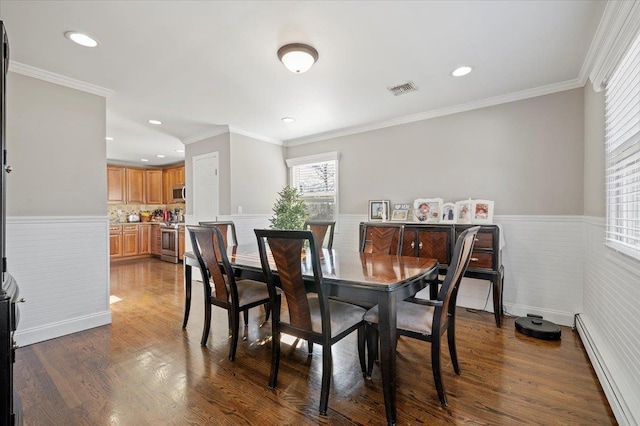 dining room featuring visible vents, dark wood-type flooring, wainscoting, crown molding, and baseboard heating