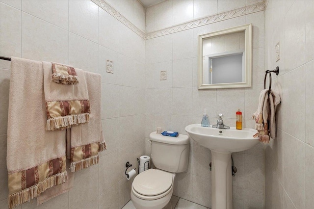 half bath featuring tile walls and toilet