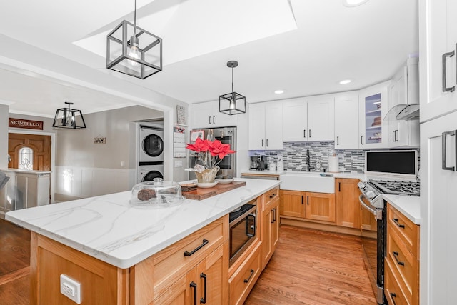 kitchen featuring stacked washer and dryer, a kitchen island, white cabinets, appliances with stainless steel finishes, and sink