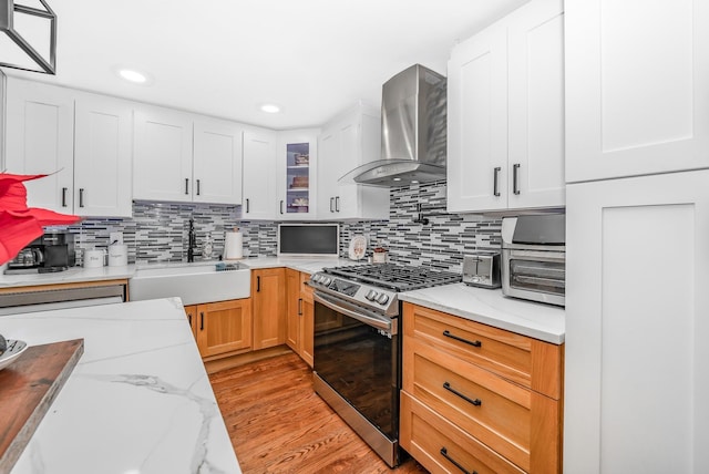 kitchen with sink, stainless steel range with gas stovetop, wall chimney range hood, and light stone countertops