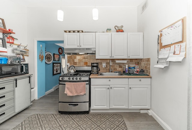 kitchen featuring stainless steel gas range oven, sink, white cabinetry, decorative light fixtures, and backsplash