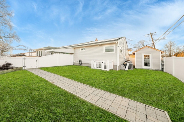 rear view of house featuring central AC unit, a lawn, and an outdoor structure