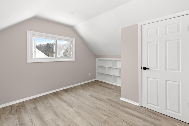 additional living space with lofted ceiling, built in shelves, and light hardwood / wood-style flooring