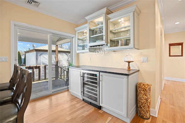 bar with ornamental molding, light hardwood / wood-style floors, beverage cooler, and white cabinets