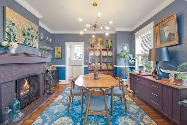 dining area with ornamental molding, dark wood-type flooring, a notable chandelier, and a fireplace