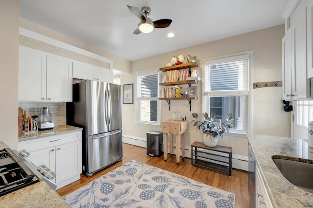 kitchen with stainless steel appliances, a baseboard radiator, light stone countertops, and white cabinets