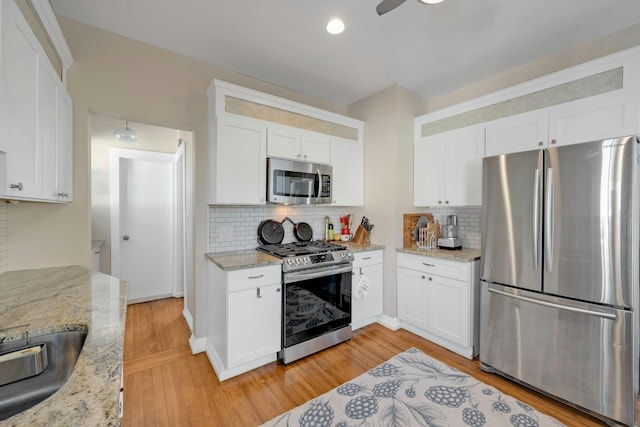 kitchen featuring stainless steel appliances, light stone countertops, white cabinets, and light wood-type flooring