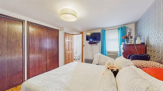 bedroom with ensuite bath, cooling unit, radiator, and two closets