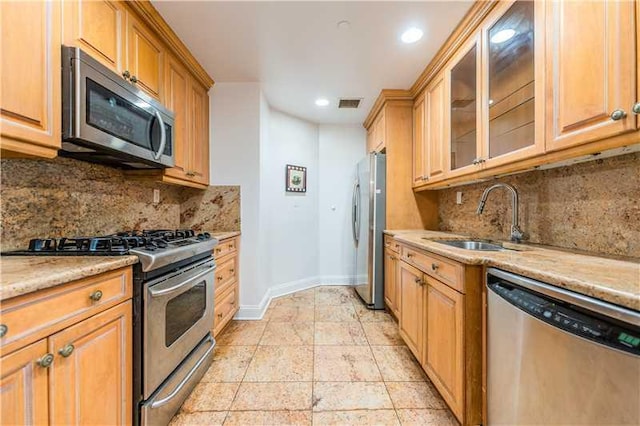 kitchen featuring decorative backsplash, appliances with stainless steel finishes, light stone counters, and sink