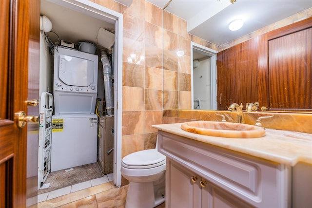 bathroom featuring stacked washing maching and dryer, vanity, tile walls, tile patterned flooring, and toilet