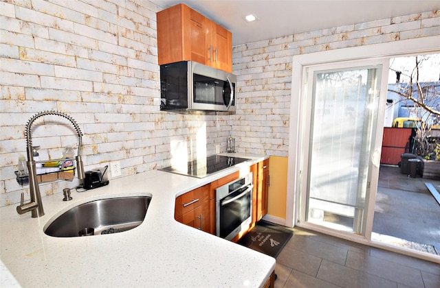 kitchen featuring brick wall, appliances with stainless steel finishes, light stone countertops, and sink