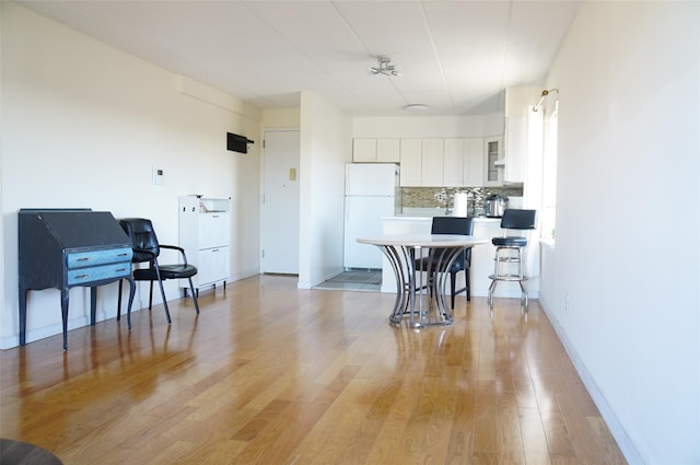 kitchen with white cabinetry, light hardwood / wood-style flooring, white refrigerator, backsplash, and a breakfast bar