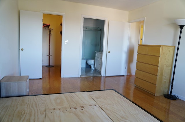 unfurnished bedroom with connected bathroom, a spacious closet, a closet, and hardwood / wood-style flooring