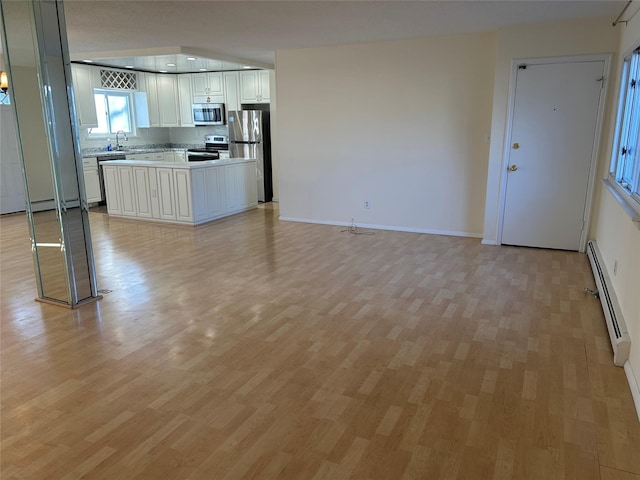 kitchen with a baseboard heating unit, sink, light wood-type flooring, tasteful backsplash, and stainless steel appliances