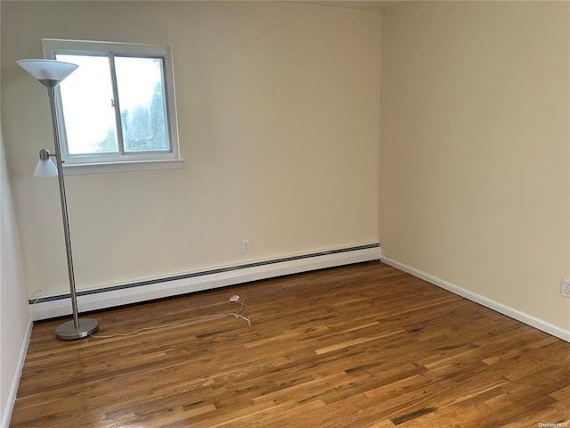 empty room featuring hardwood / wood-style floors and a baseboard heating unit