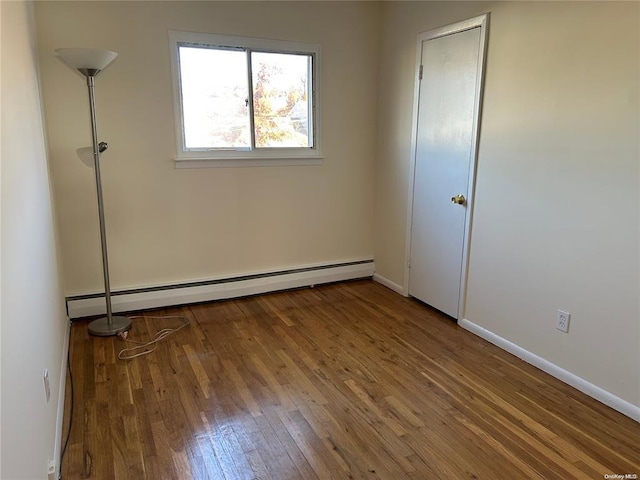 unfurnished room featuring hardwood / wood-style flooring and a baseboard heating unit