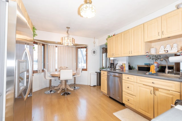 kitchen featuring stainless steel appliances, hanging light fixtures, light brown cabinets, sink, and light hardwood / wood-style flooring