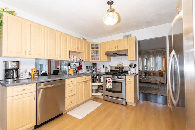 kitchen featuring appliances with stainless steel finishes, light wood-type flooring, pendant lighting, sink, and tasteful backsplash