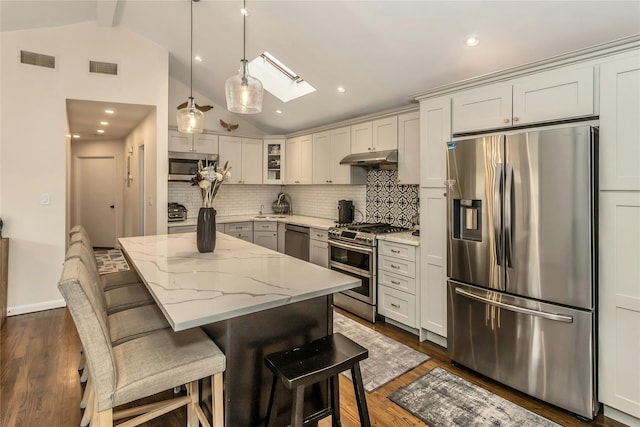 kitchen with a kitchen bar, appliances with stainless steel finishes, light stone counters, vaulted ceiling with skylight, and white cabinetry