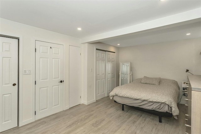 bedroom with light hardwood / wood-style flooring and multiple closets