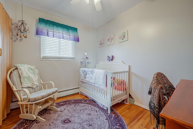 bedroom with ceiling fan, wood-type flooring, a nursery area, and a baseboard heating unit